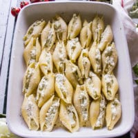 large shells with ricotta mixture stuffed inside all layered on a white baking dish.