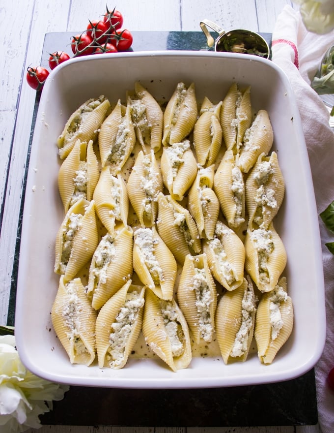 large shells with ricotta mixture stuffed inside all layered on a white baking dish.
