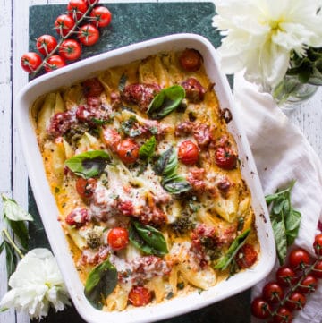 finished ricotta stuffed shells dish in a white baking dish on a table with tomatoes and flowers.