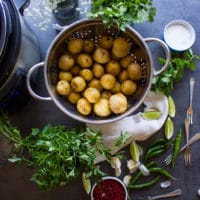 ingredients to make pan fried potatoes recipe ingredient including raw pottaoe sin a colander, lots of fresh herbs, garlic, spices, lime wedges