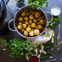 ingredients to make pan fried potatoes recipe ingredient including raw pottaoe sin a colander, lots of fresh herbs, garlic, spices, lime wedges