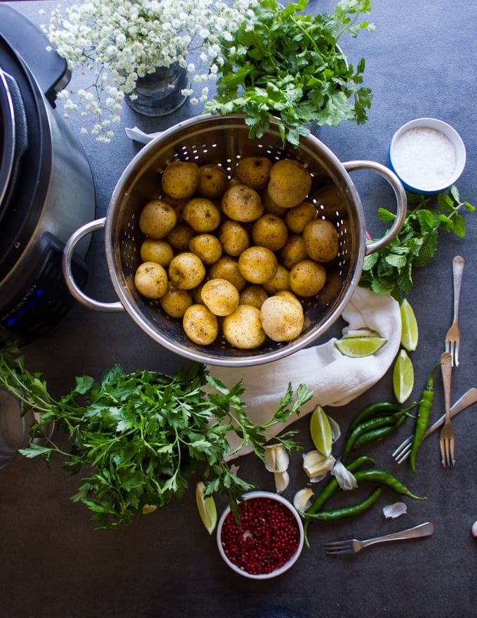 ingredients to make pan fried potatoes recipe ingredient including raw pottaoe sin a colander, lots of fresh herbs, garlic, spices, lime wedges