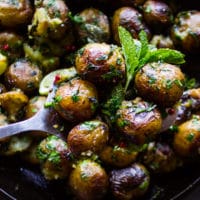 A spoon holding a few pan fried potatoes showing the crisp and herbs