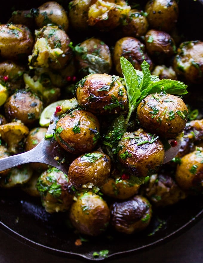 A spoon holding a few pan fried potatoes showing the crisp and herbs