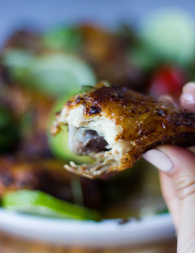 A hand holding a bitten piece of air fryer chicken legs showing the succuelnt cooked chicken and the crispy skin