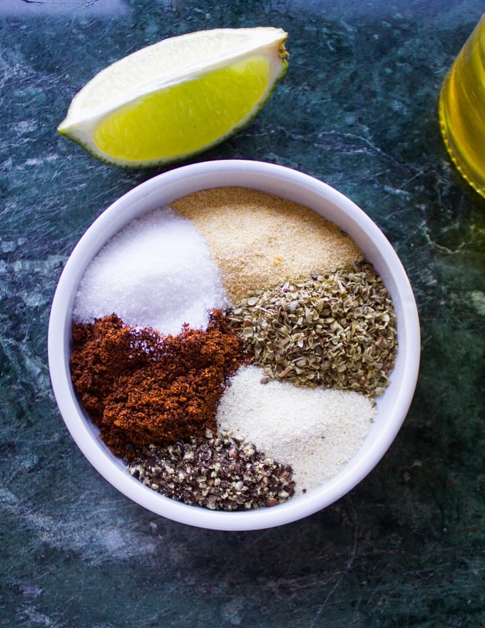 a mall plate with al the spices needed for the chicken including, garlic powder, onion powder, chilli powder, salt, pepper and oregano