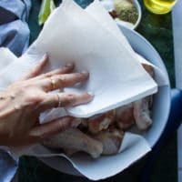 A hand patting the chicken legs dry using kitchen towels