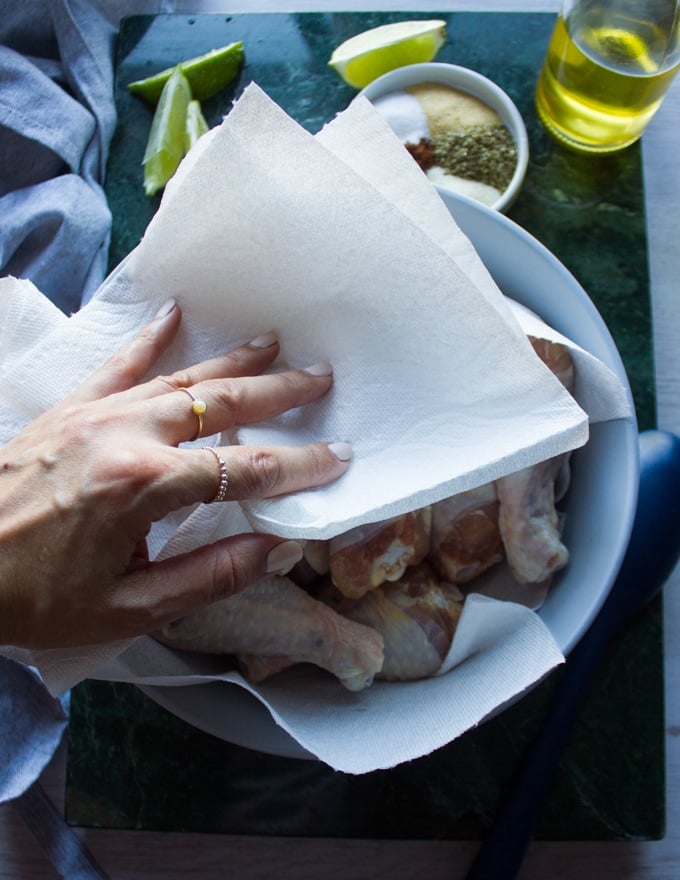 A hand patting the chicken legs dry using kitchen towels