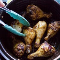 A hand flipping the chicken legs half way during air frying to ensure even cooking of the chicken legs