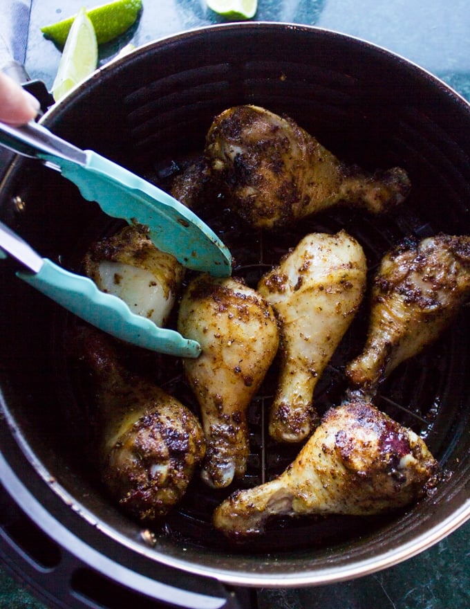 A hand flipping the chicken legs half way during air frying to ensure even cooking of the chicken legs