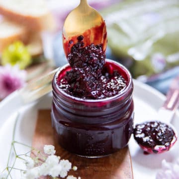 A spoon dripping from a blackberry jam jar showing the color and texture of the jam