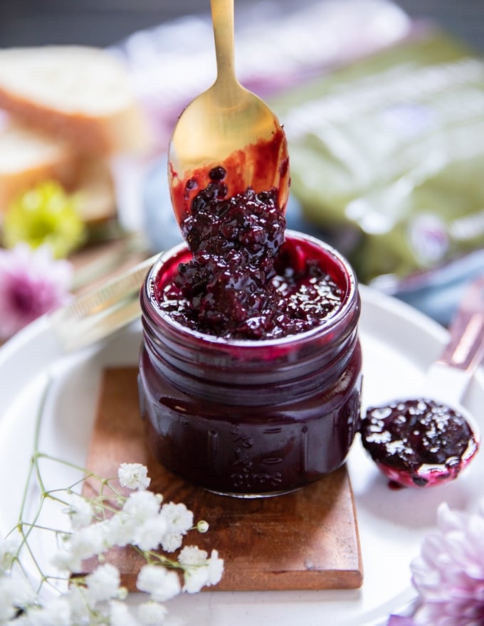 A spoon dripping from a blackberry jam jar showing the color and texture of the jam