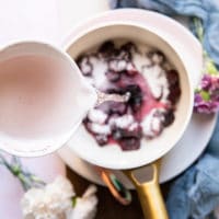 A bowl of water pouring into a pot with the marionberry blackberry and sugar ready to simmer