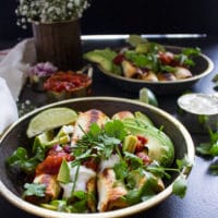 a plate of chicken flautas cooked and ready, topped with salsa, avocado, sour cream and lots of cilantro