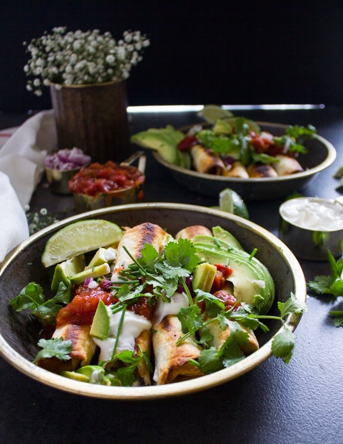 a plate of chicken flautas cooked and ready, topped with salsa, avocado, sour cream and lots of cilantro 