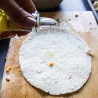 tortillas on a wooden board and hand pouring some old over the tortillas to make sure to coat them well