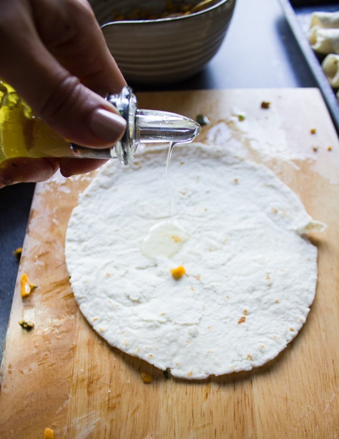 tortillas on a wooden board and hand pouring some old over the tortillas to make sure to coat them well