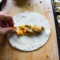 Chicken and cheese filling being placed in the center of the tortilla and ready to be rolled out into flautas