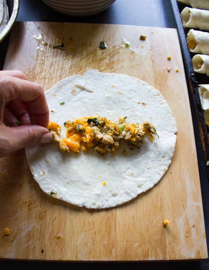 Chicken and cheese filling being placed in the center of the tortilla and ready to be rolled out into flautas