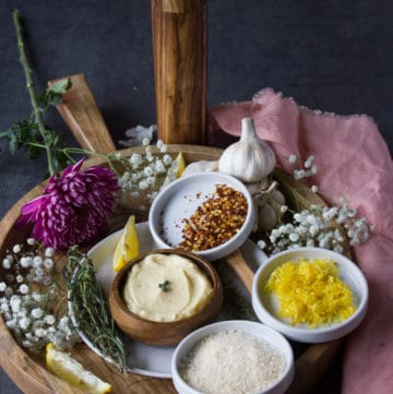 The garlic butter sauce on a tray surrounded with small bowls of flavoring such as chilli flakes, lemon zest, parmesan cheese, herbs and lemon wedges