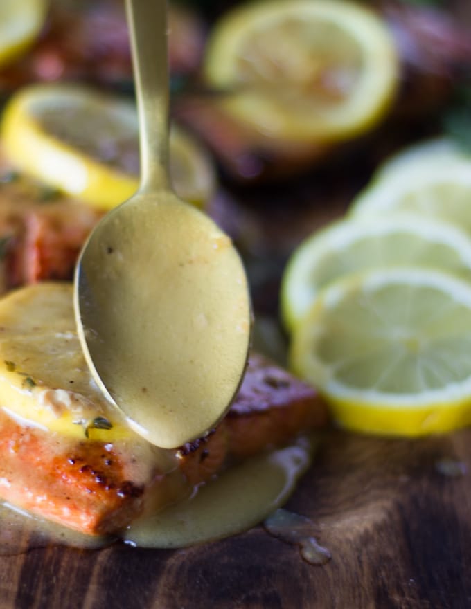 sockeye salmon on a plate and a hand drizzling the lemon butter sauce over the cooked sockeye salmon recipe