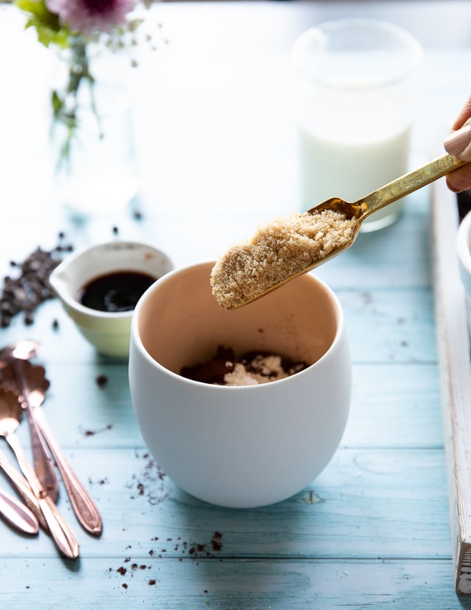 A spoon adding in the brown sugar to the mug to make brownie in a mug