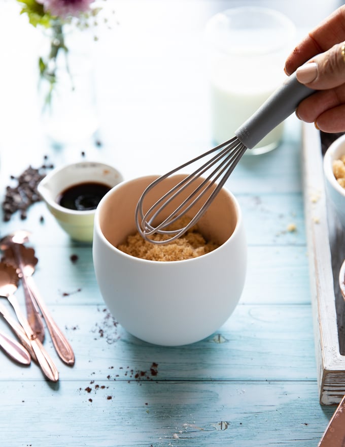 A hand holding a small whisk to whisk in the dry ingredients in the mug to make brownies