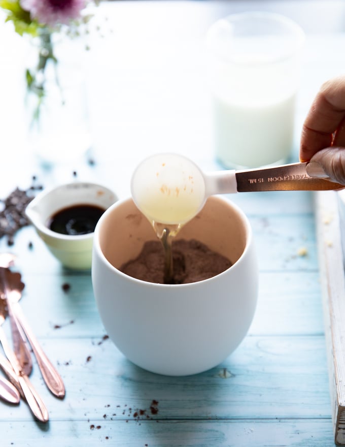 A tablespoon of oil being added to the mug using a tablespoon