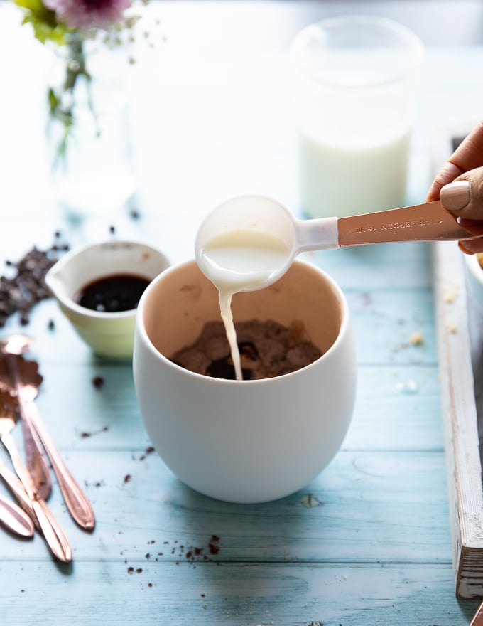 A spoonful of milk added to the mug to make the brownie in a mug batter 