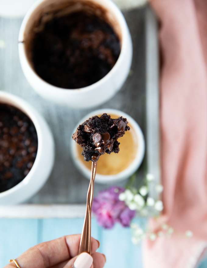 A spoon holding a brownie cooked in a mug loaded with chocolate chips melting and gooey