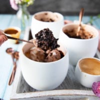 A spoon holding off a brownie from the mug with ice cream and caramel sauce showing the fudgy texture of brownies