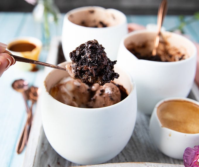 A spoon holding off a brownie from the mug with ice cream and caramel sauce showing the fudgy texture of brownies