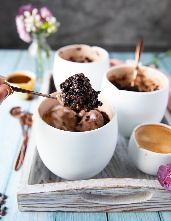 A spoon holding off a brownie from the mug with ice cream and caramel sauce showing the fudgy texture of brownies