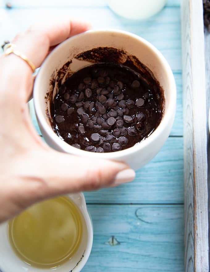 A hand holding a brownie in a mug ready to go in the micowave