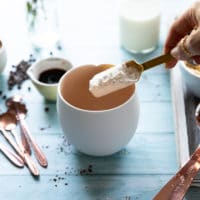 A hand spooning in flour in the mug to make a brownie in a mug