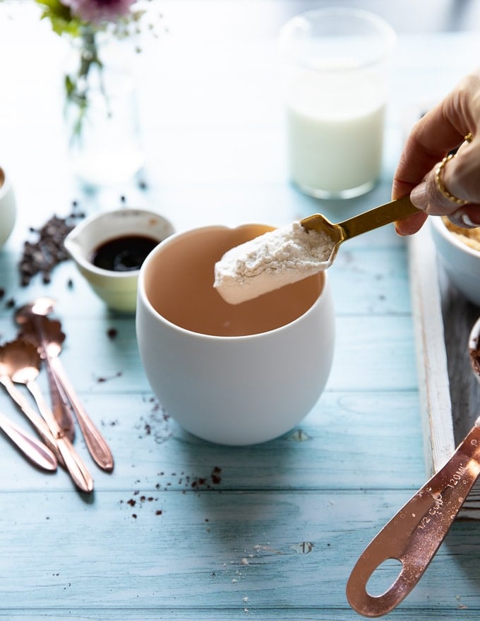 A hand spooning in flour in the mug to make a brownie in a mug