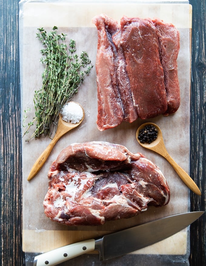 two different cuts of meats to make the philly cheesesteak recipe, bith partially frozen for easy slicing and placed on a paper over the wooden table