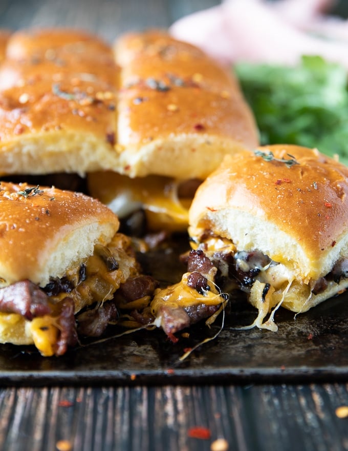 three philly cheese steak sliders with the filling showing off the cookes meat and veggies and cheese
