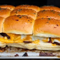 Philly cheesesteak sliders on the grill showing close up of the cheese melting and the sliders ready to eat