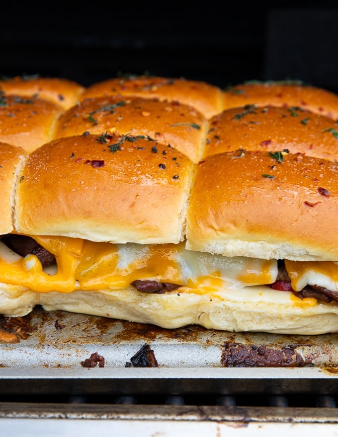 Philly cheesesteak sliders on the grill showing close up of the cheese melting and the sliders ready to eat