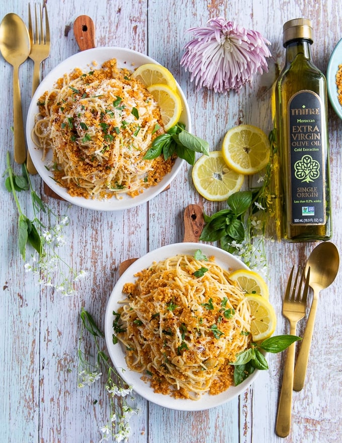 two bowls of spaghetti aglio e olio or olive oil pasta with forks and spoons and a lenon slices on the side with fresh basil and Moroccan olive oil