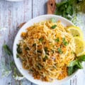 A single plate of spaghetti aglio e olio with lemon slices on the side and some fresh basil leaves