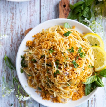 A single plate of spaghetti aglio e olio with lemon slices on the side and some fresh basil leaves