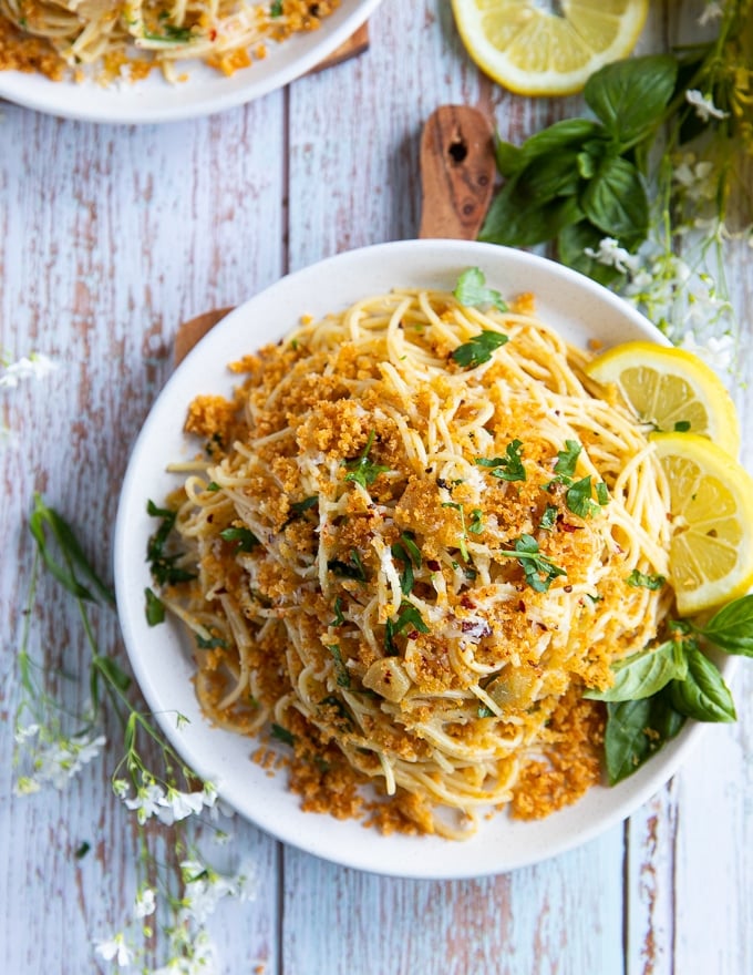 A single plate of spaghetti aglio e olio with lemon slices on the side and some fresh basil leaves