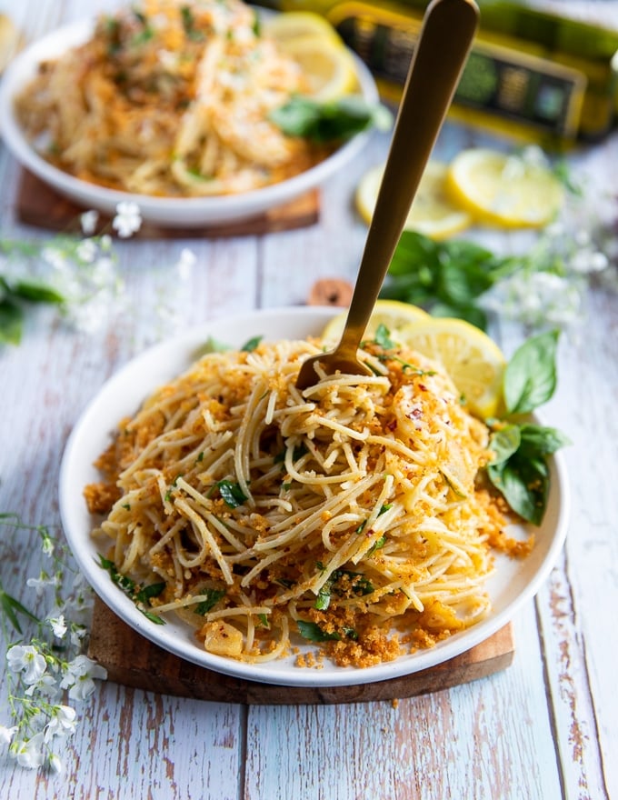 A fork swirling the spaghetti with olive oil sauce in a bowl 