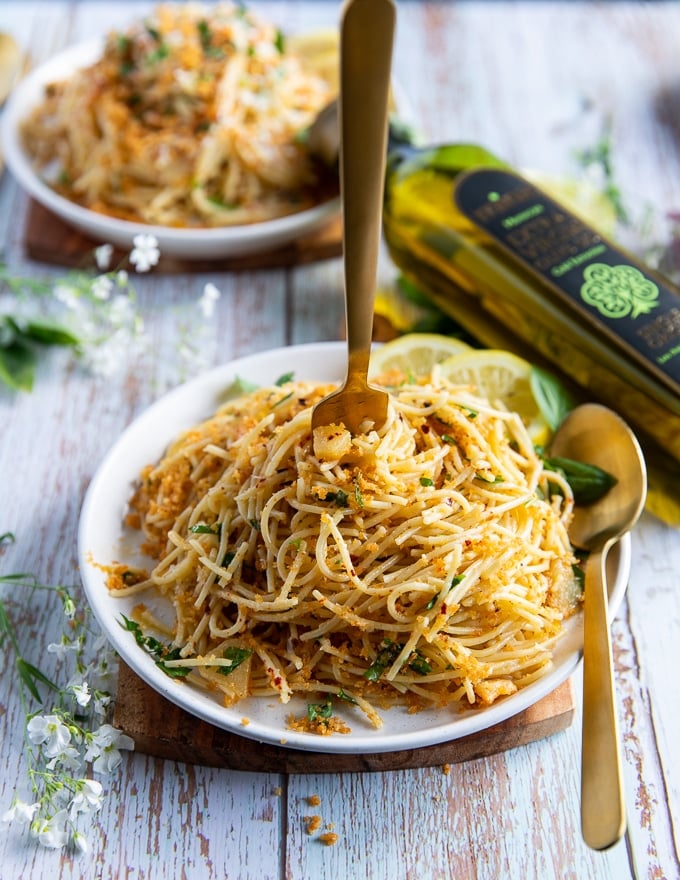 a hand eating some olive oil pasta with a fork and spoon swirling the spaghetti aglio e olio around showing the garlic, olive oil, basil and read crumbs