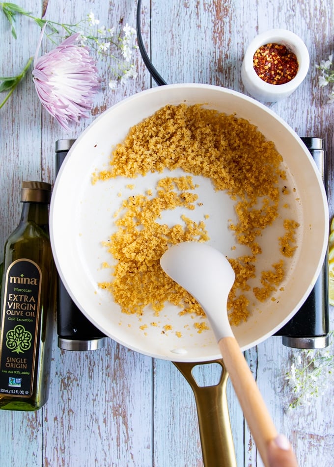 A spatula tossing the bread crumbs in a skillet until toasty and ready