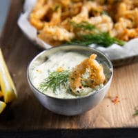 A dipped fried calamari in tartar sauce with a piece of dill