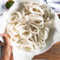 A hand holding a plate of sliced squid rings showing what is calamari