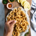 A hand holding a piece of calamari over a plate of fried calamari showing the crispy texture